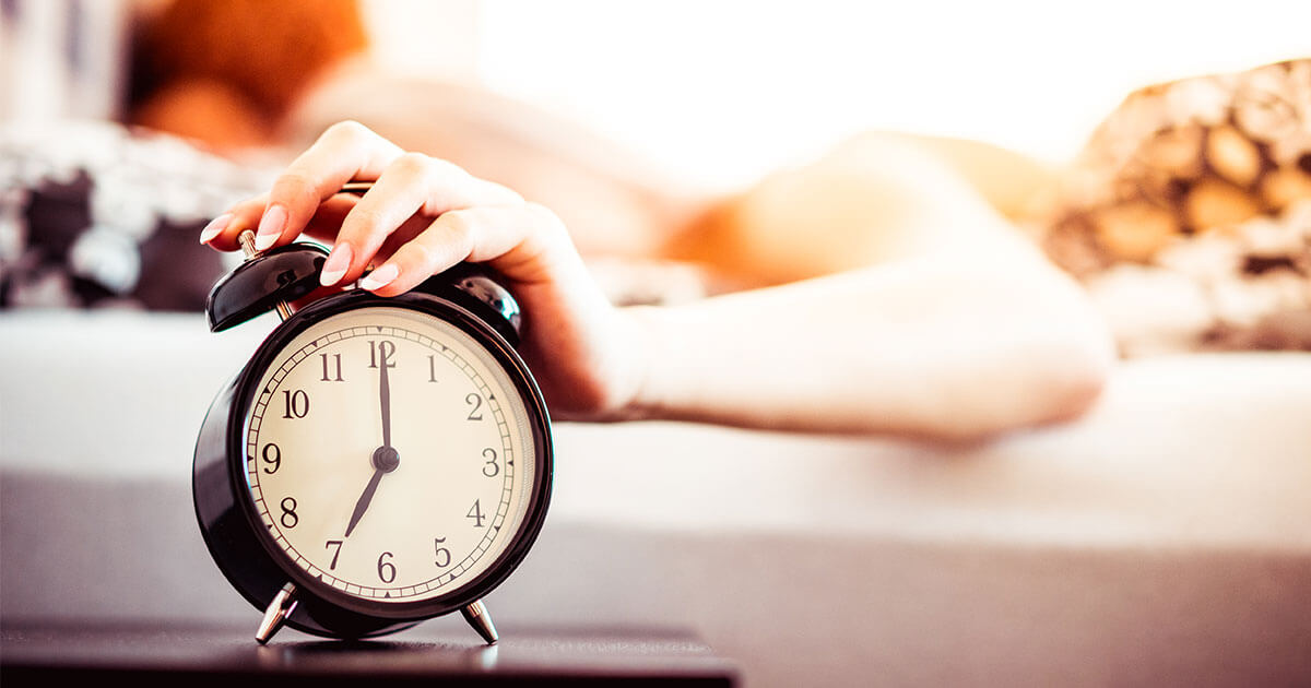 ベッドの上で目覚まし時計を止める女性